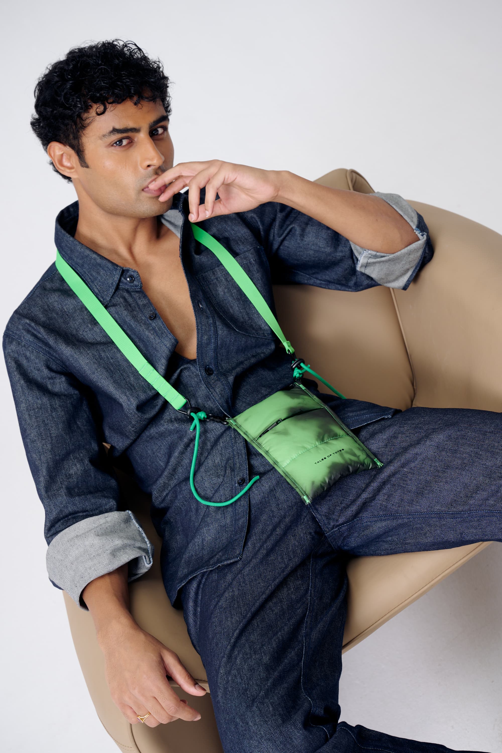 Man sitting on a beige chair wearing a blue outfit with green accents.
