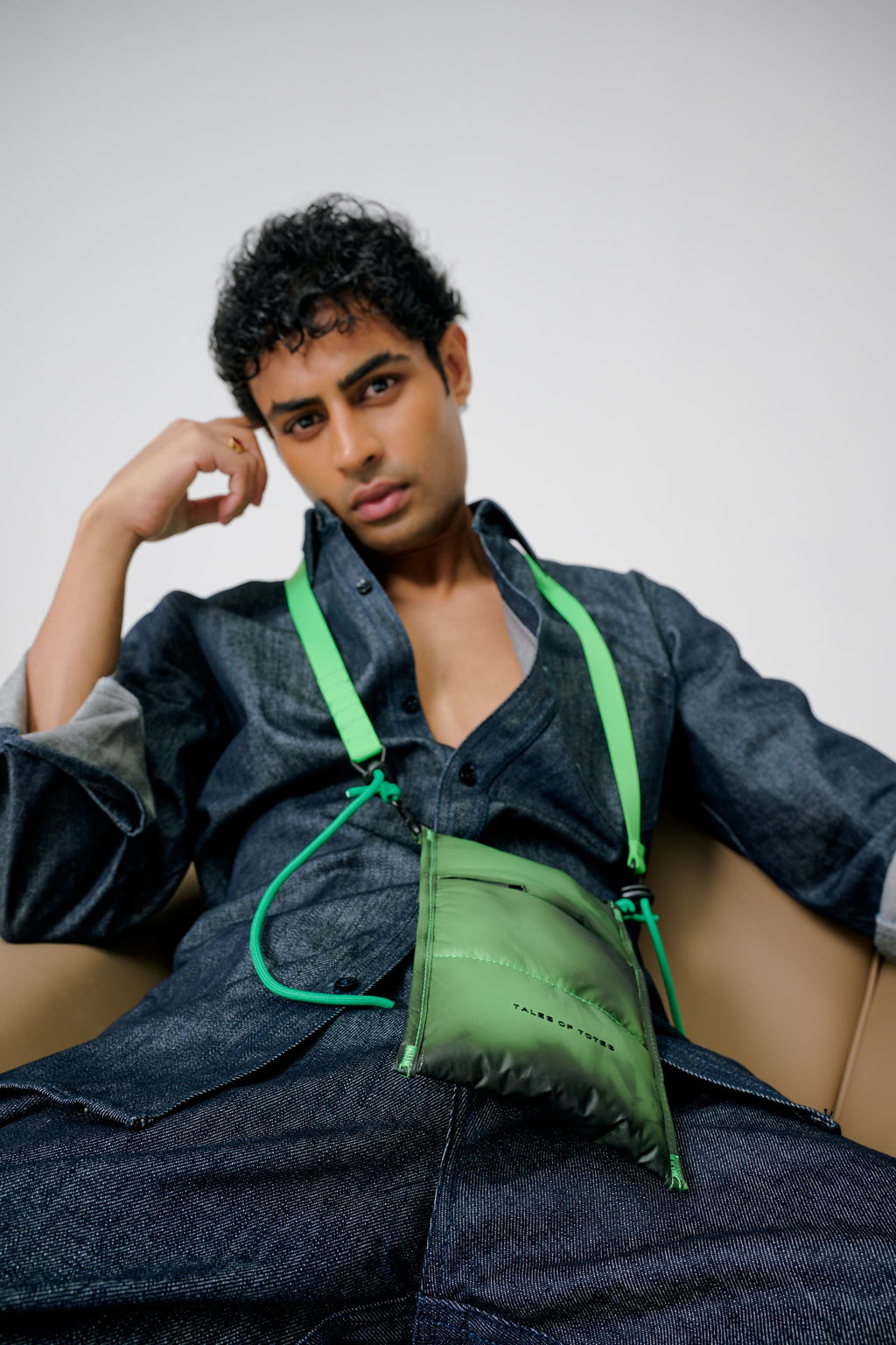 Man wearing a green bag over his shoulder against a plain background