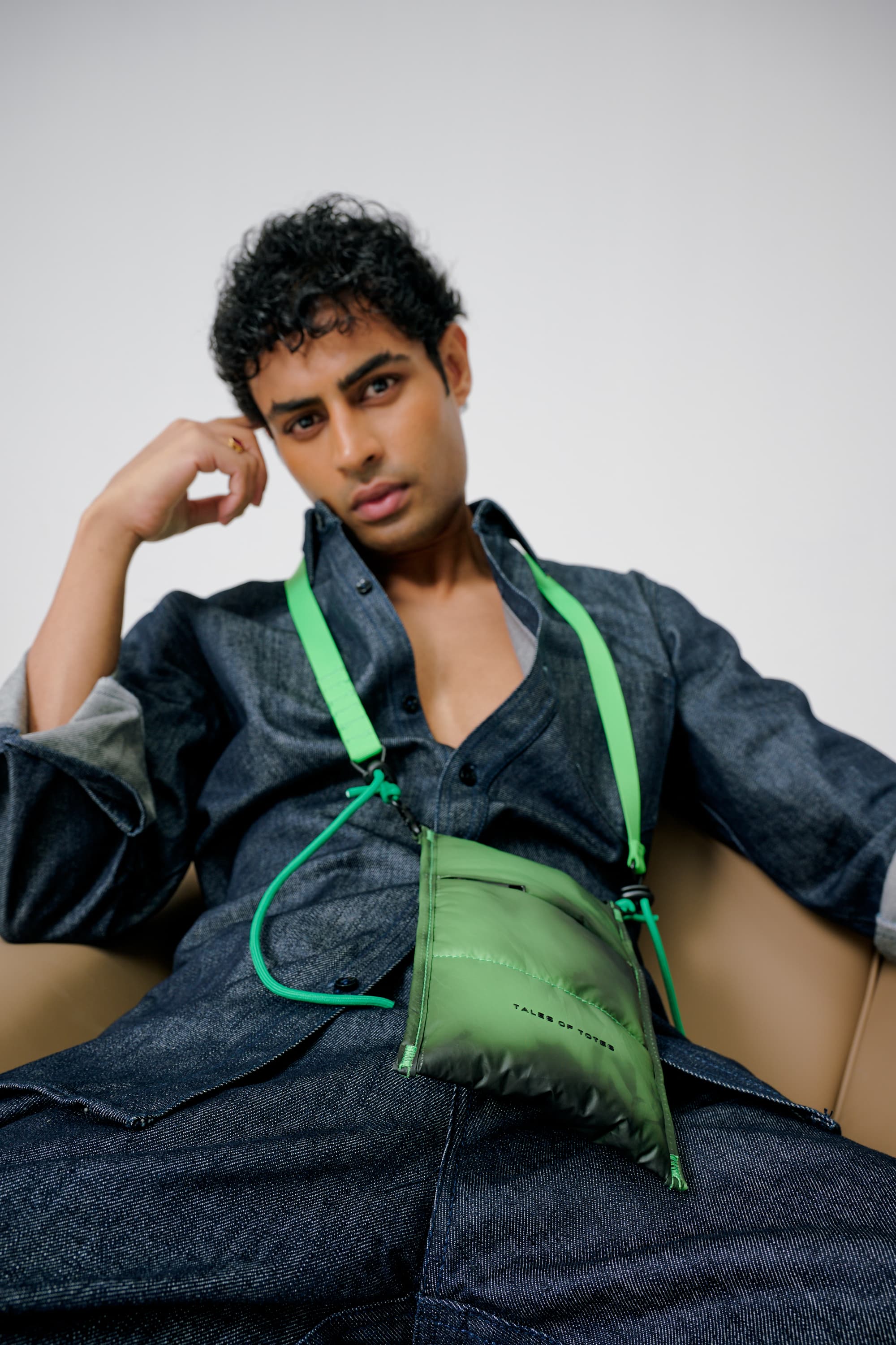 Man wearing a green bag over his shoulder against a plain background