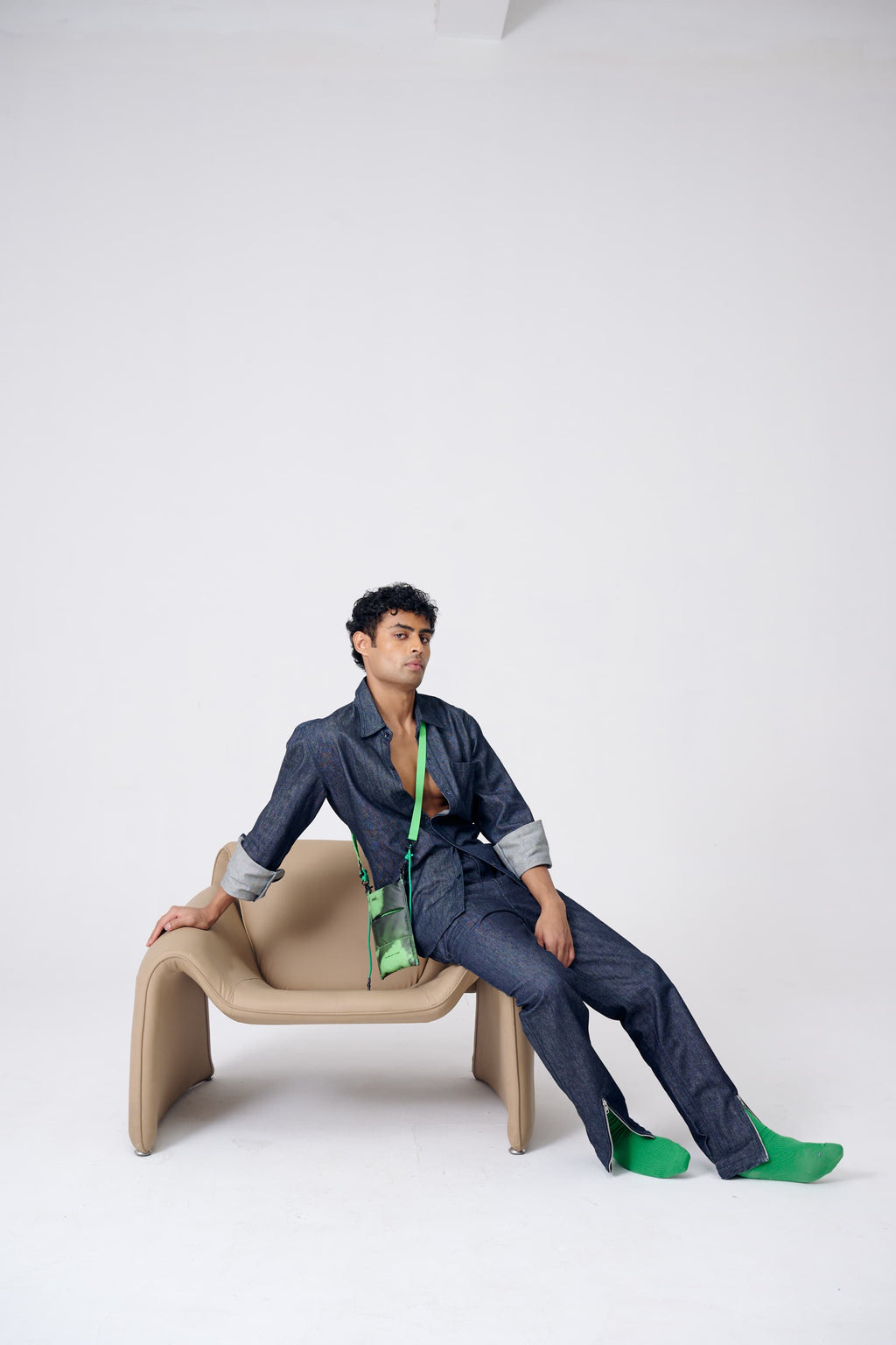 Person sitting on a modern chair wearing a blue outfit with green shoes and a green scarf.