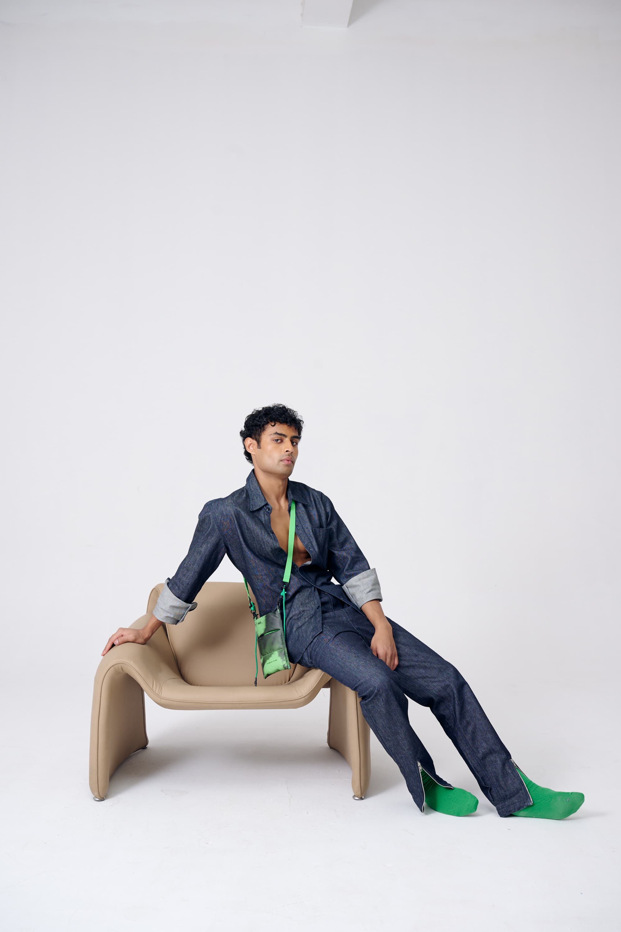 Person sitting on a modern chair wearing a blue outfit with green shoes and a green scarf.