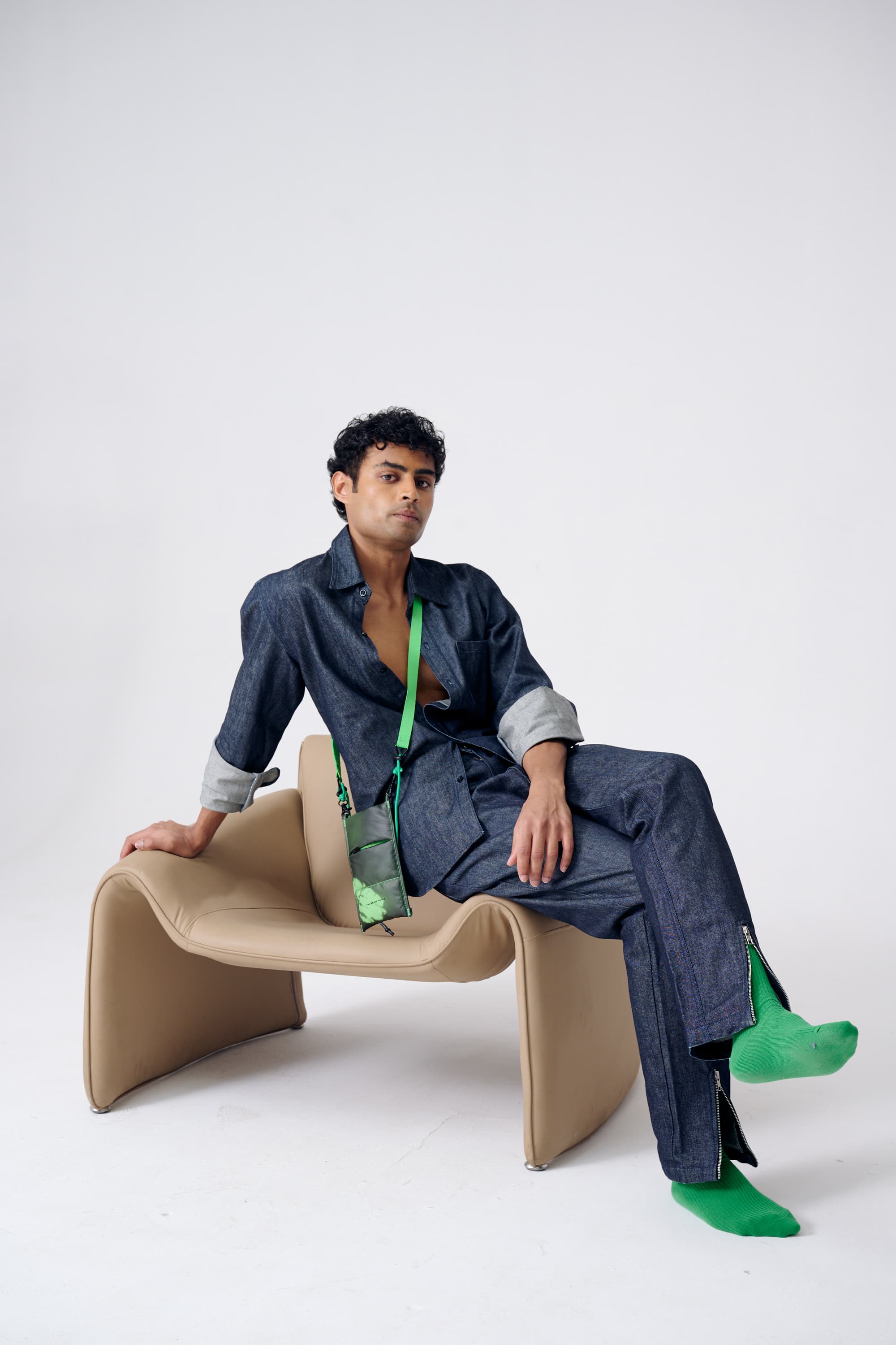 Man in a blue outfit sitting on a modern chair against a white background