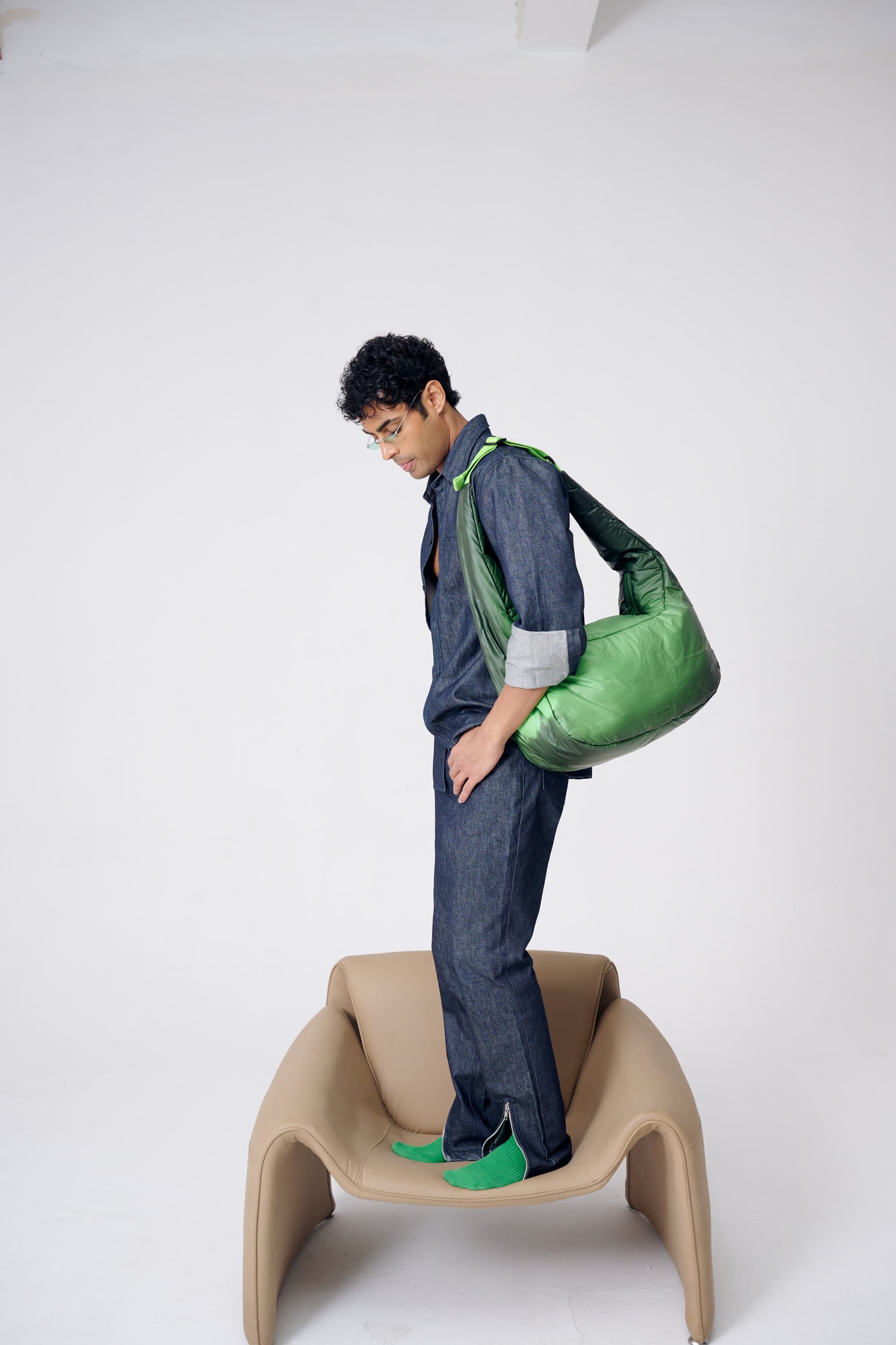 Person standing on a chair holding a green bag against a white background