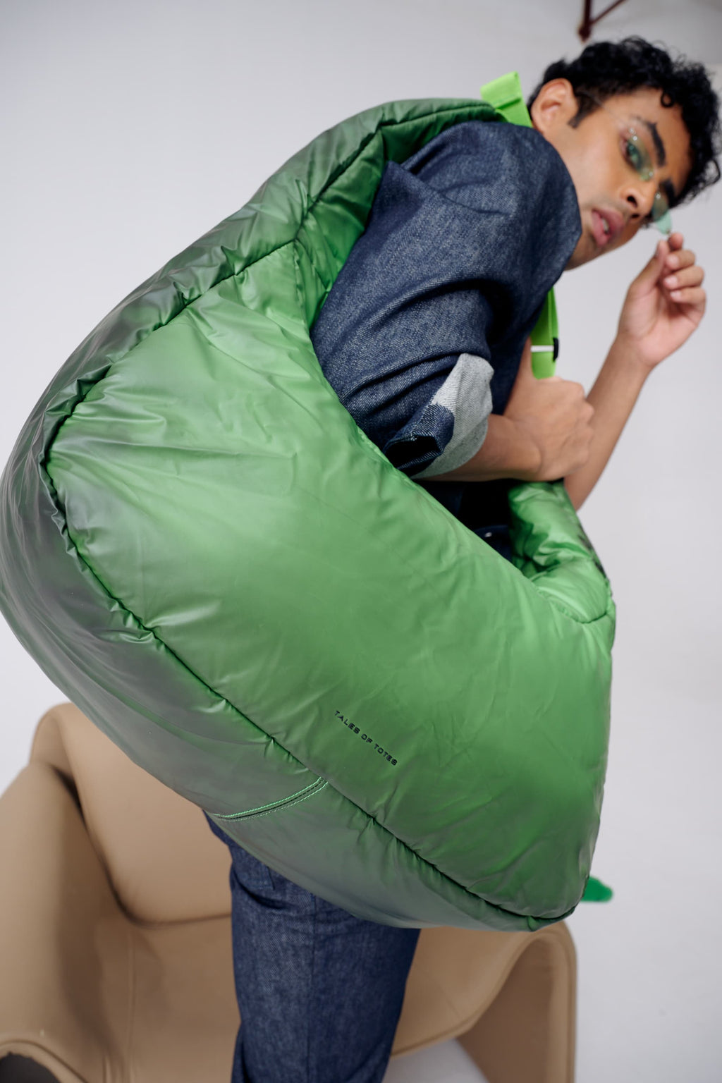 Person wearing a large green sleeping bag over their head on a white background