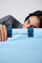 Person peeking out from behind a blue tote bag with 'Tales of Totes' branding.