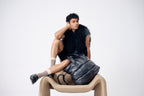 Man sitting on a chair with a black bag over his lap against a white background