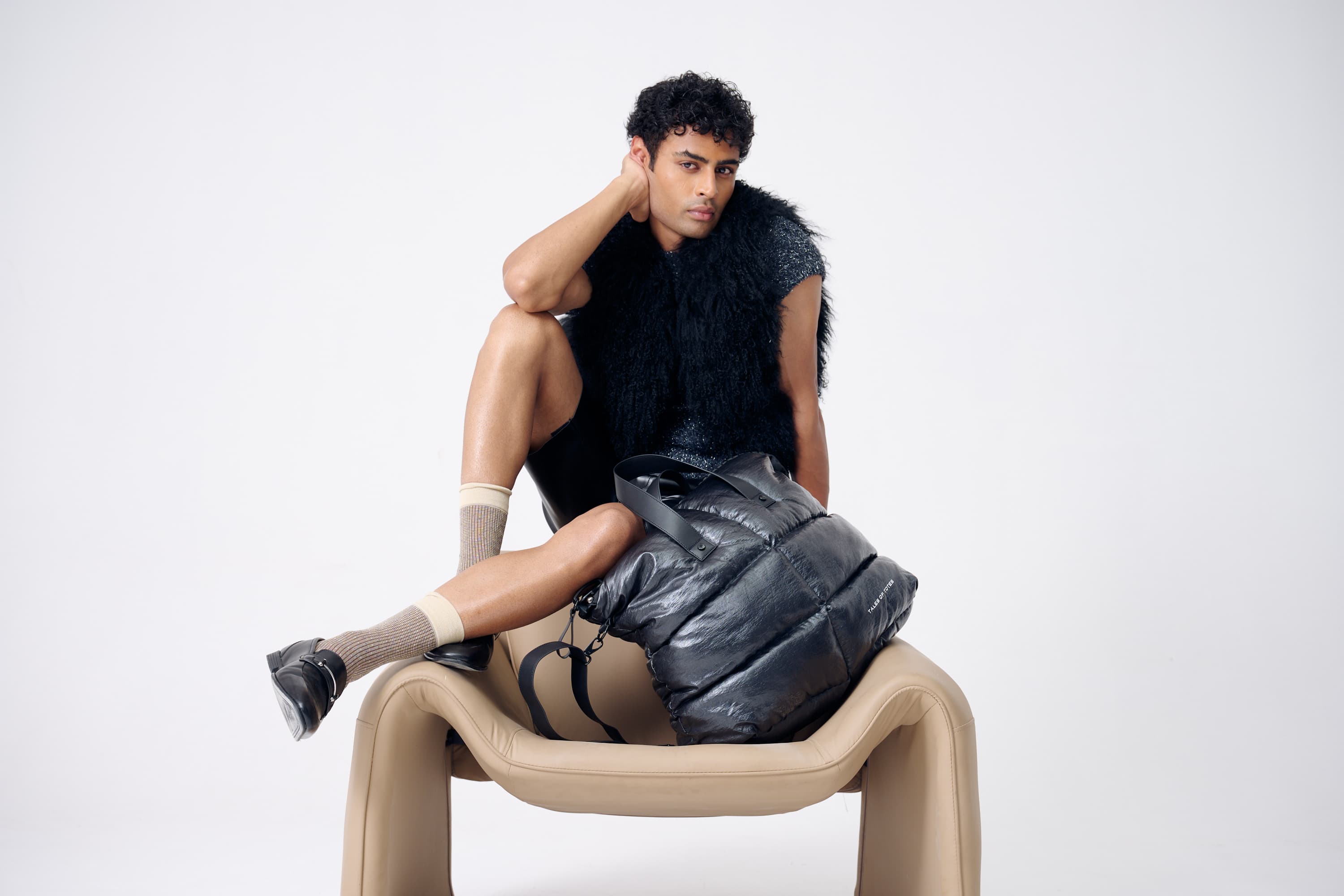 Man sitting on a modern chair wearing a sleeveless top and pants with a white background