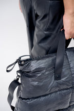 Person holding a dark gray puffer bag with a plain background