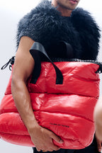 Person holding a red puffer bag with black fur trim against a white background