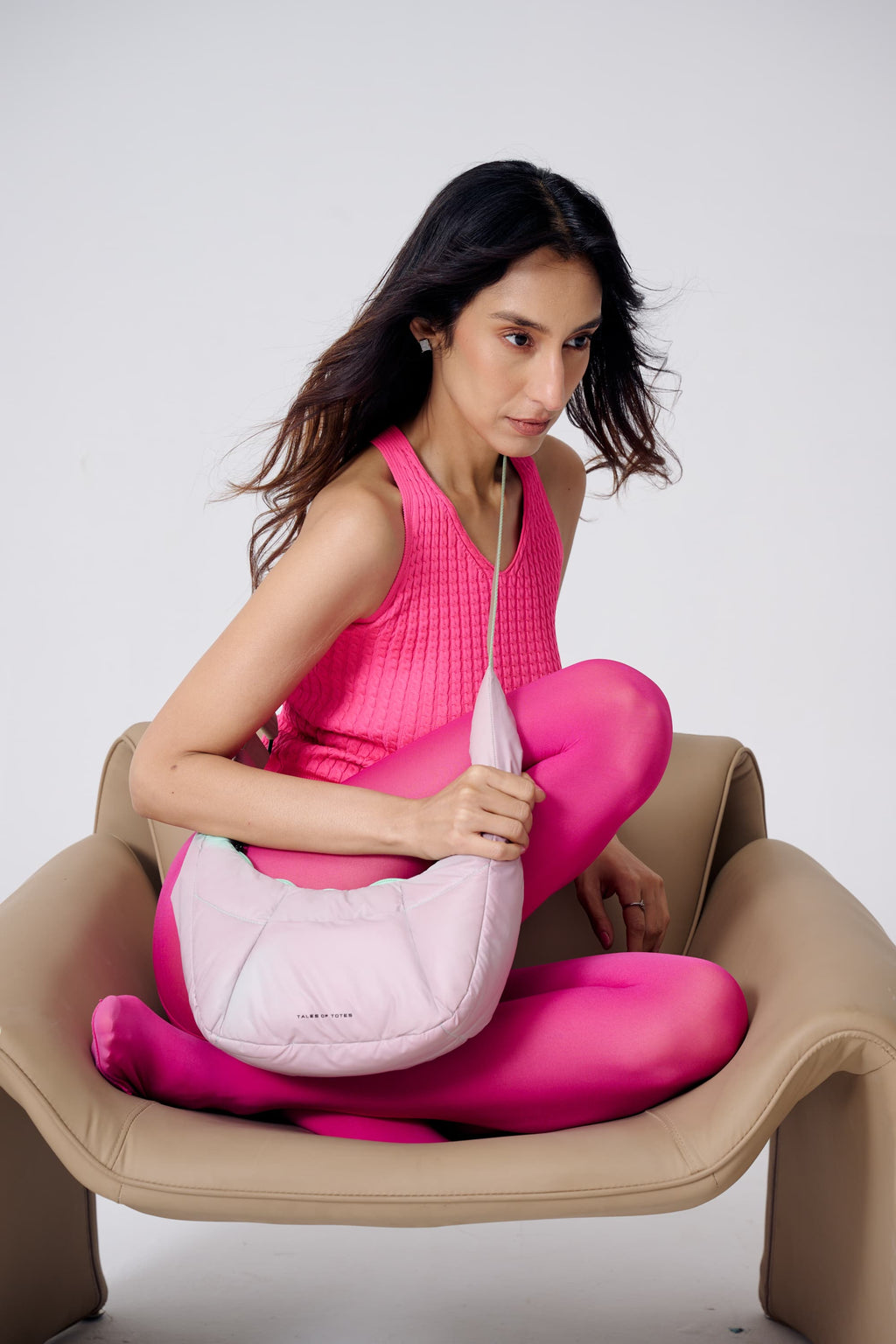 Woman in pink outfit holding a white bag on a beige chair against a white background