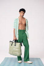 Man wearing a green and white striped shirt and green pants, holding a light green bag on a checkered floor.