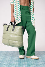 Person wearing green pants and holding a green puffer bag on a tiled floor.