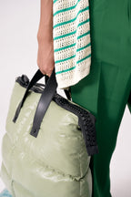 Person holding a light green puffer bag with black straps against a white background