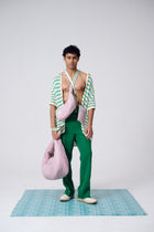 Man holding a pink bag wearing a green outfit on a checkered floor with a white background