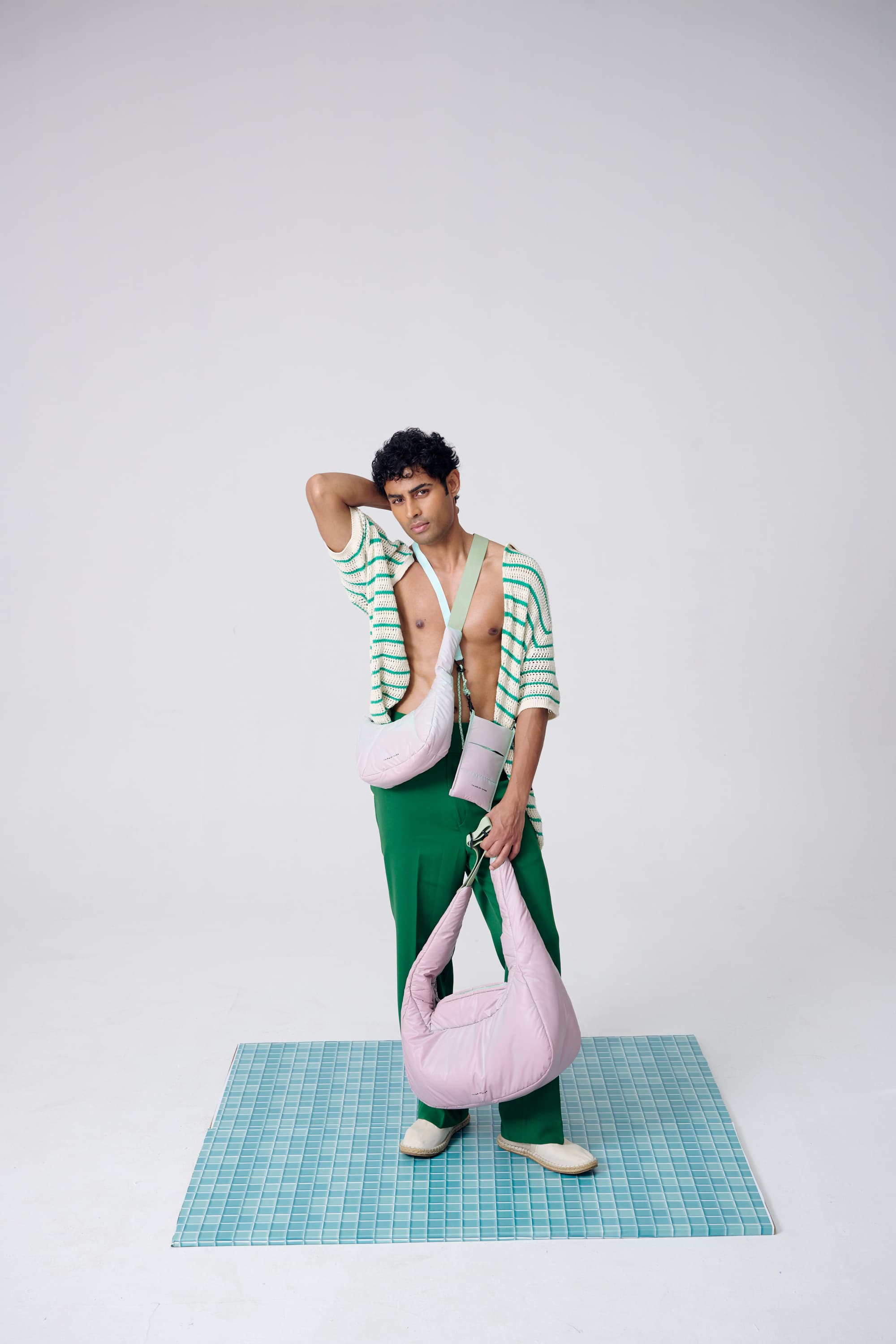 Person wearing a green and white striped shirt with rolled-up sleeves, holding pink bags on a checkered floor.