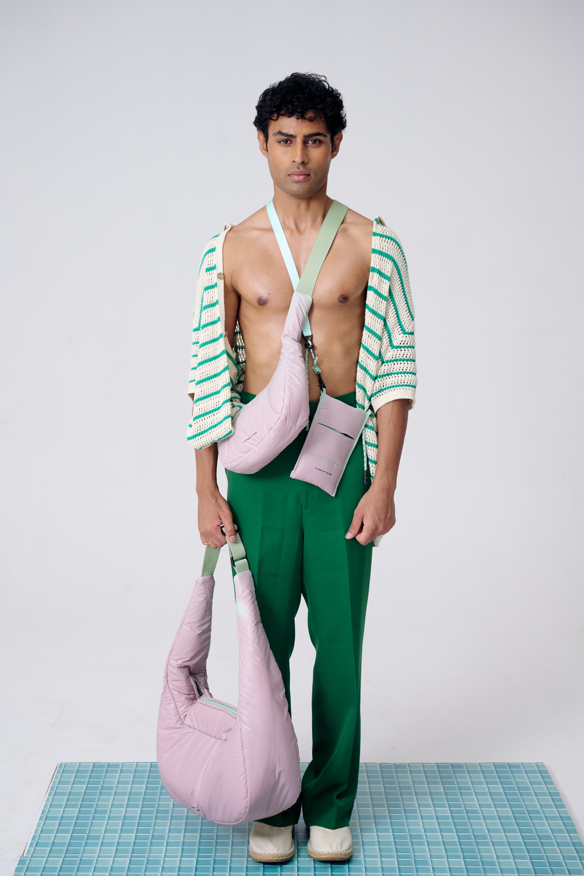 Man wearing a green and white striped shirt with green pants, holding pink bags on a checkered floor.