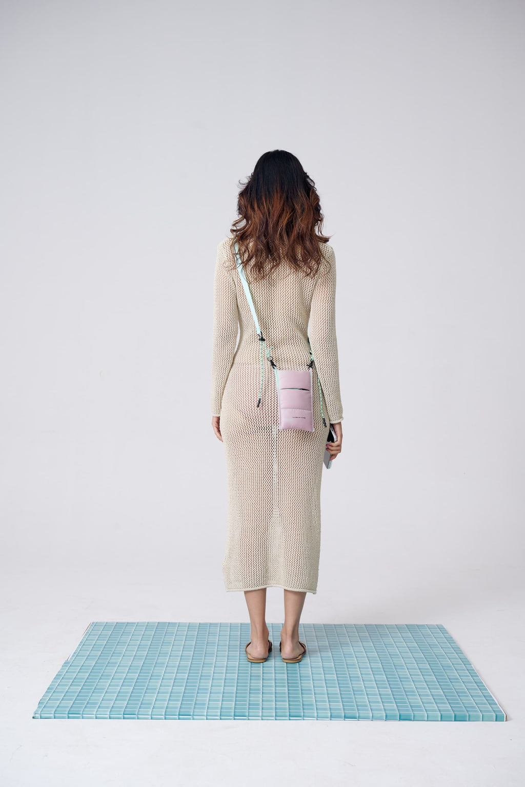 Woman in a beige dress with a pink bag standing on a blue grid mat against a white background