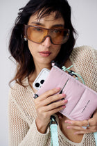 Woman holding a pink wallet and phone with a plain background