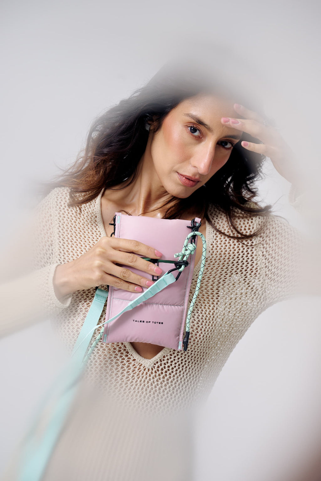 Woman holding a pink handbag with a strap against a neutral background