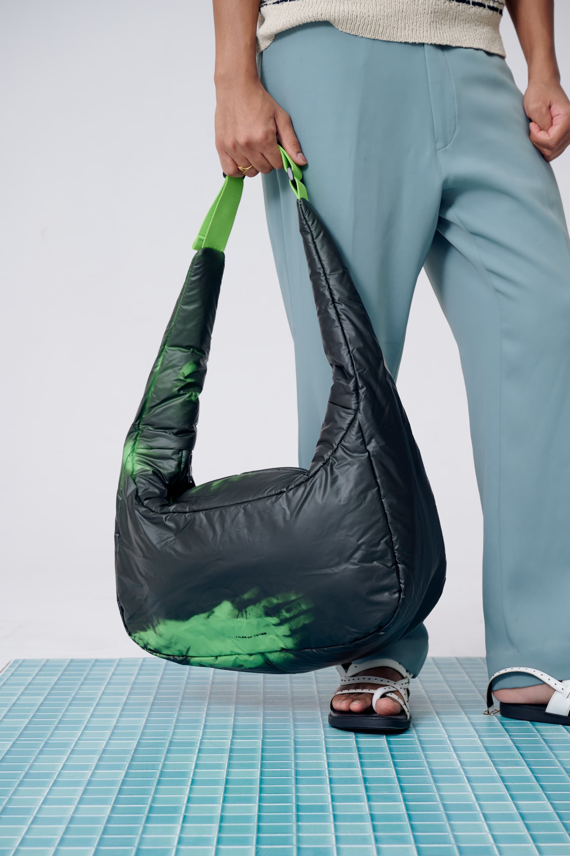 Person holding a black and green bag on a tiled floor