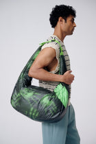 Person carrying a green and black patterned bag on a plain background