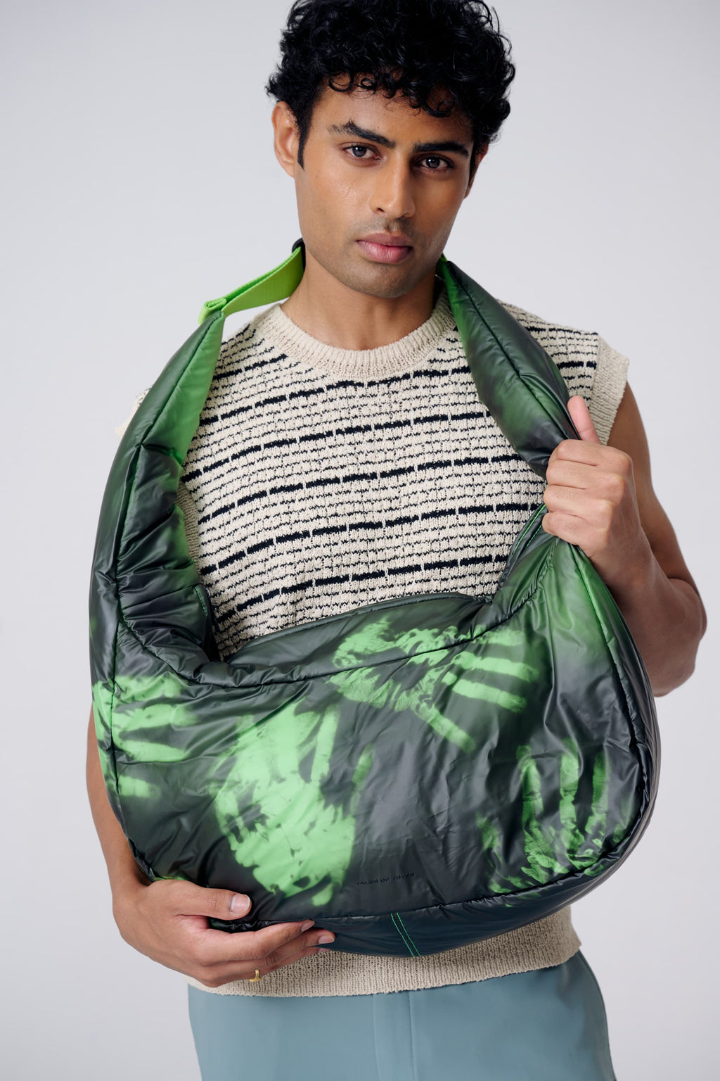 Man holding a green and black patterned bag against a plain background