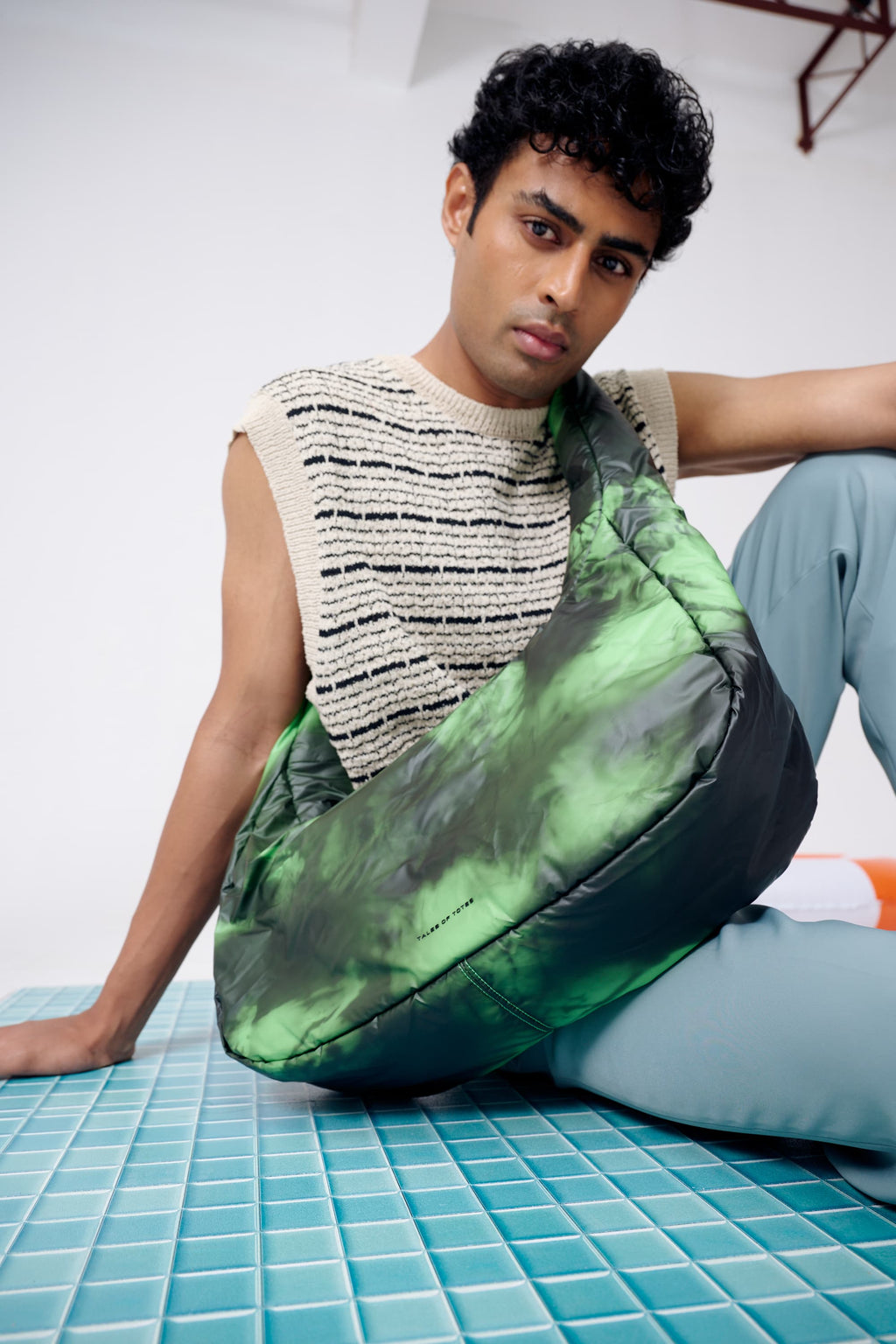 Person sitting on a green and black bean bag chair in a minimal indoor setting.