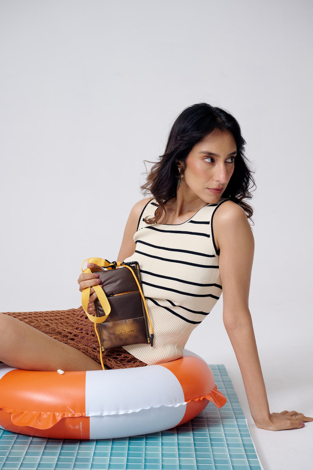 Woman sitting on a pool float holding a bag, wearing a striped swimsuit.