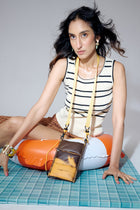 Woman sitting on a blue tiled floor with an orange bag and a yellow strap.