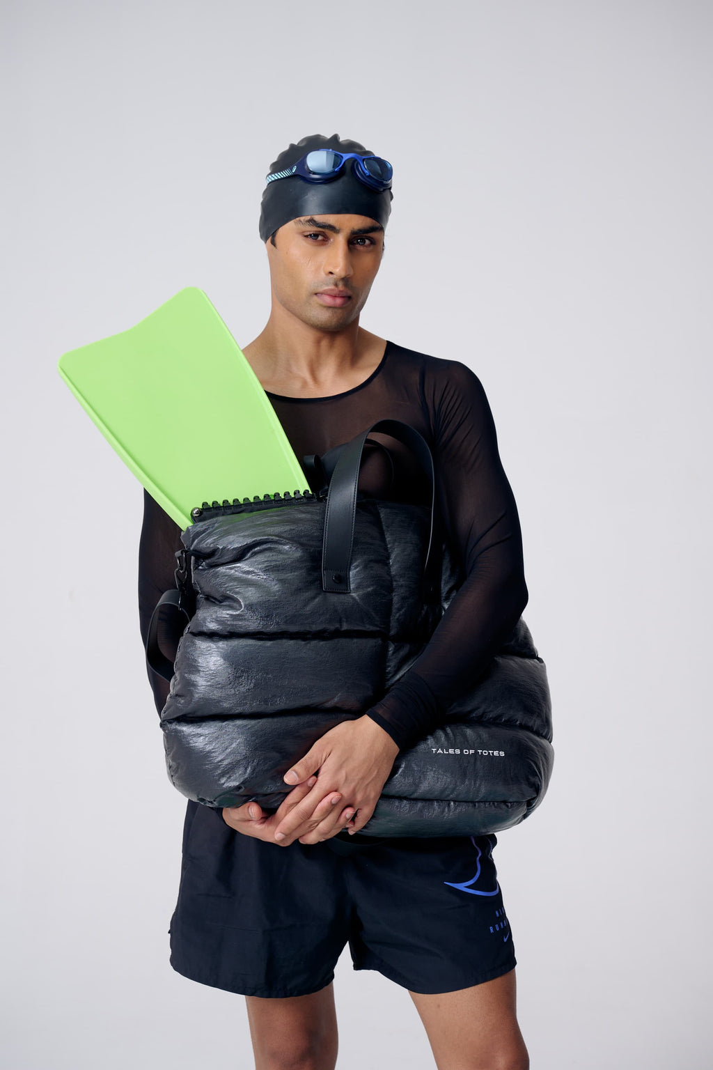 Man holding a black pack with a green folder, wearing a black outfit and headband.