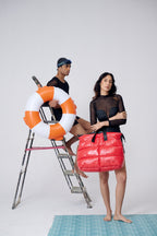 Two people with a life buoy and red bag on a ladder against a white background