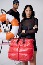 Person holding a red puffer bag with a person holding an orange life buoy in the background.