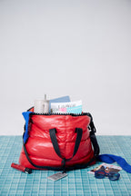 Red backpack with items like a notebook and sunglasses on a blue tiled surface.