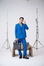 Man in a blue suit holding a black bag in a studio setting with photography equipment.