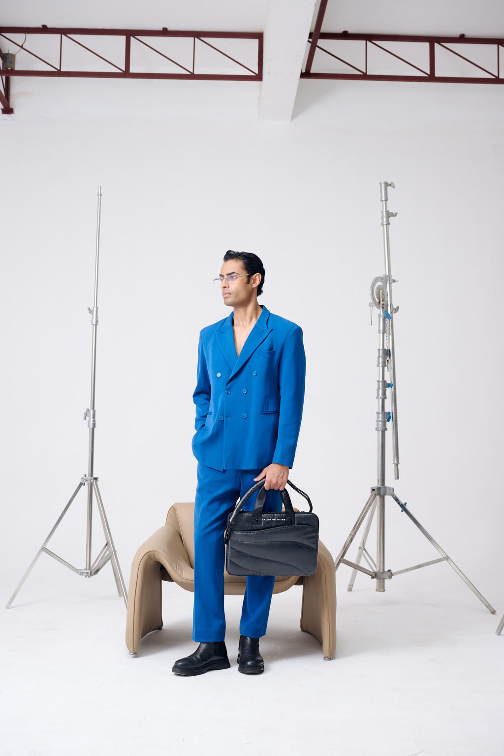 Man in a blue suit holding a black bag in a studio setting with photography equipment.
