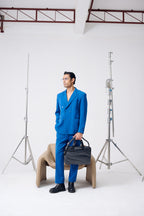 Man in a blue suit holding a black bag in a studio setting with photography equipment.