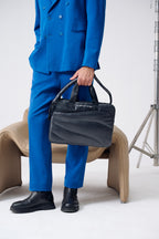 Person in a blue suit holding a black handbag on a white background