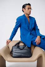 Man in a blue suit sitting on a beige chair with a black briefcase.