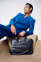 Man in a blue coat sitting on a beige chair with a black briefcase.