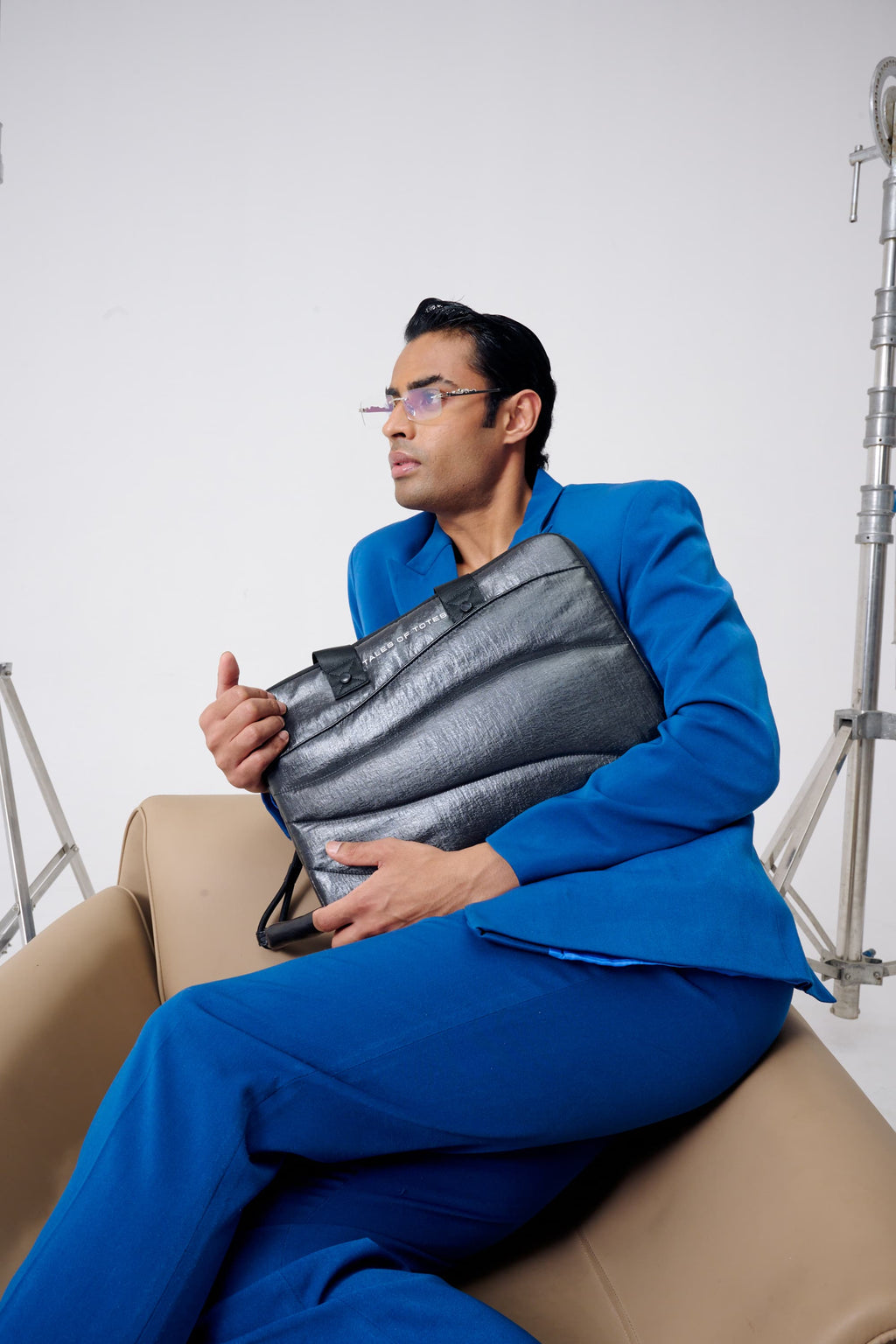 Man in a blue suit holding a gray bag on a beige chair with a white background