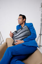 Man in a blue suit holding a gray bag on a beige chair with a white background