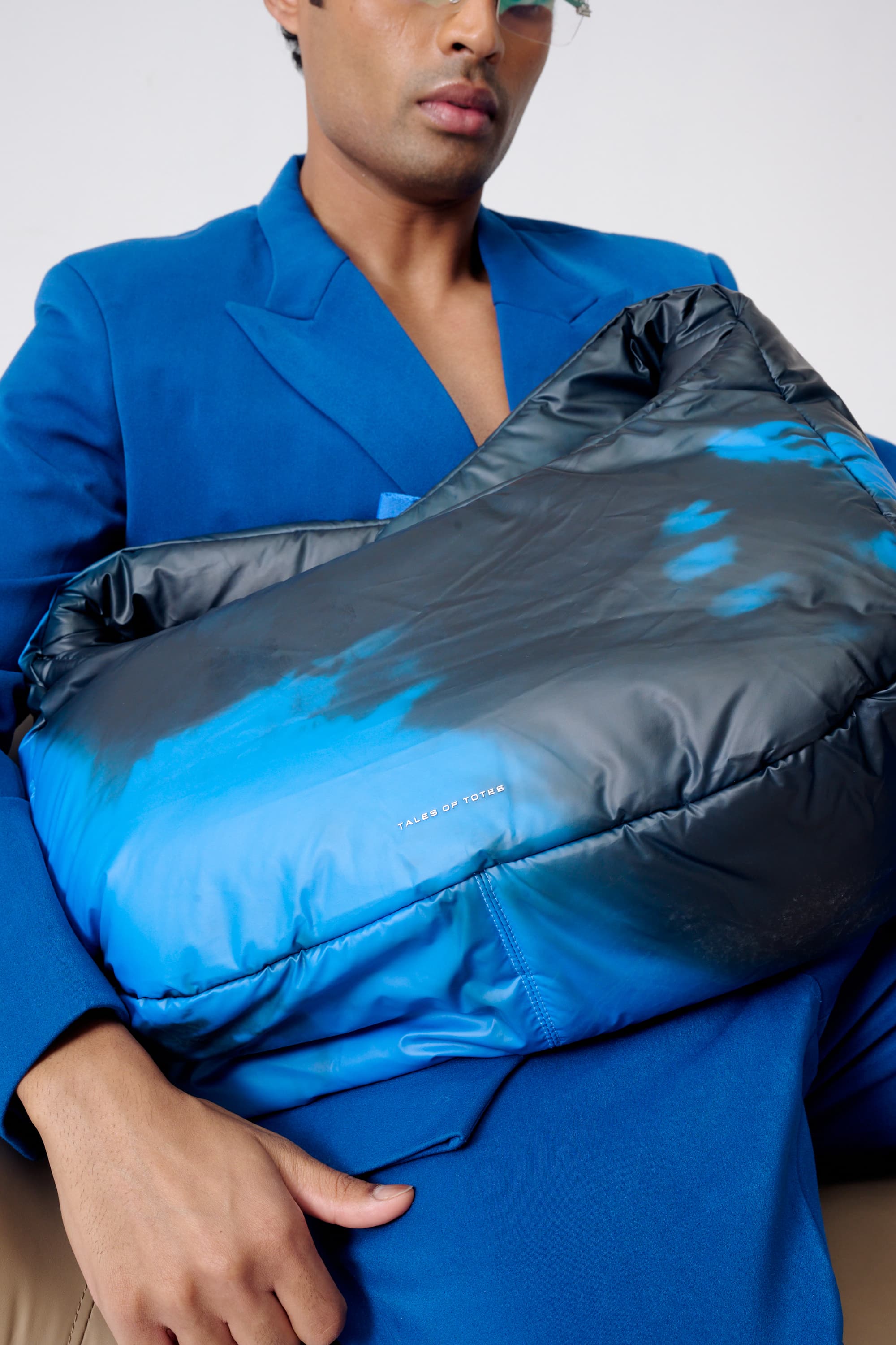 Person holding a blue and black puffer jacket against a neutral background