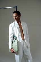 Man in a white suit holding a green handbag against a gray background