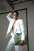 Man in a white suit holding a green bag against a plain background