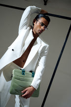 Man in a white suit holding a green clutch against a neutral background