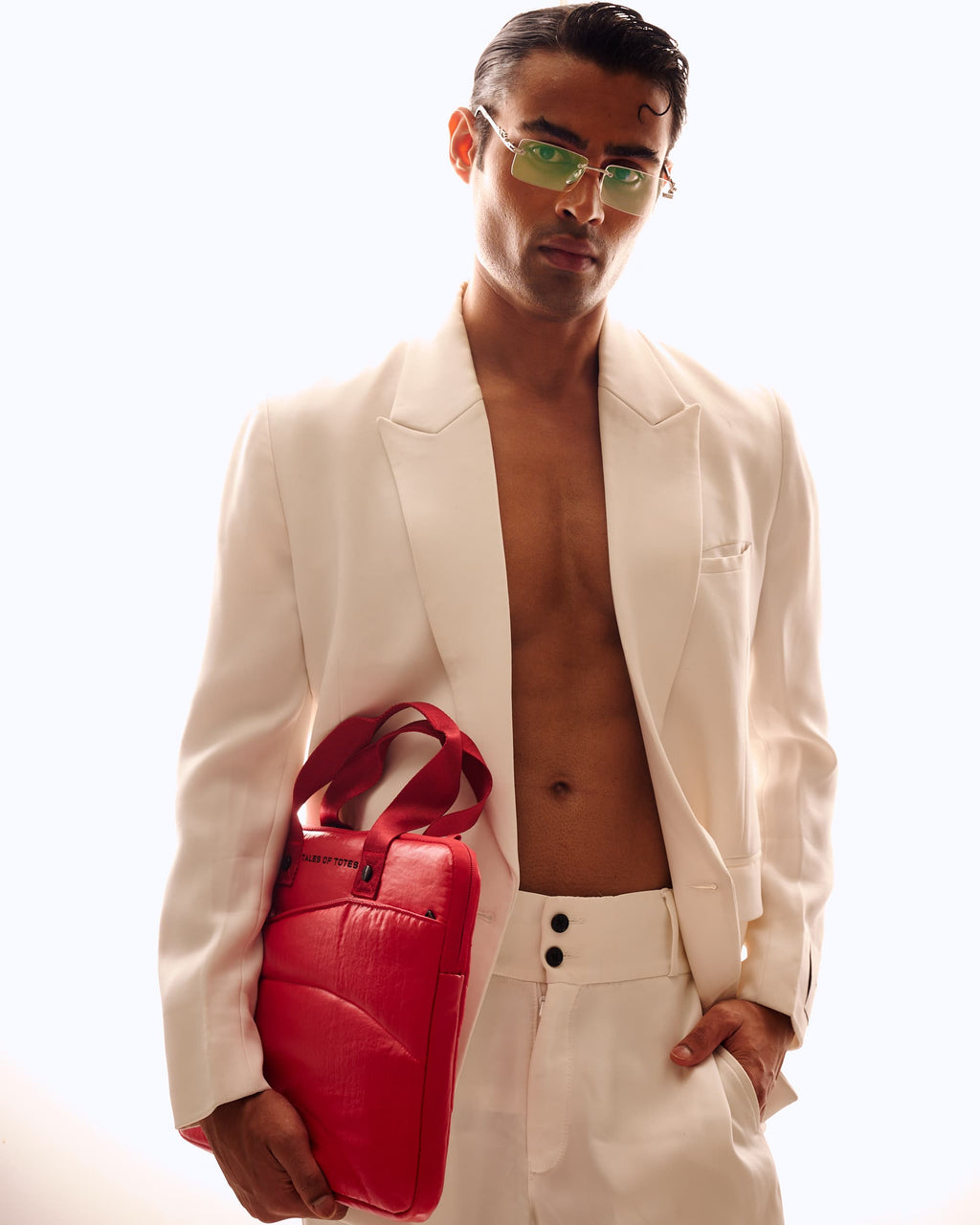 Man wearing a white suit holding a red bag against a white background