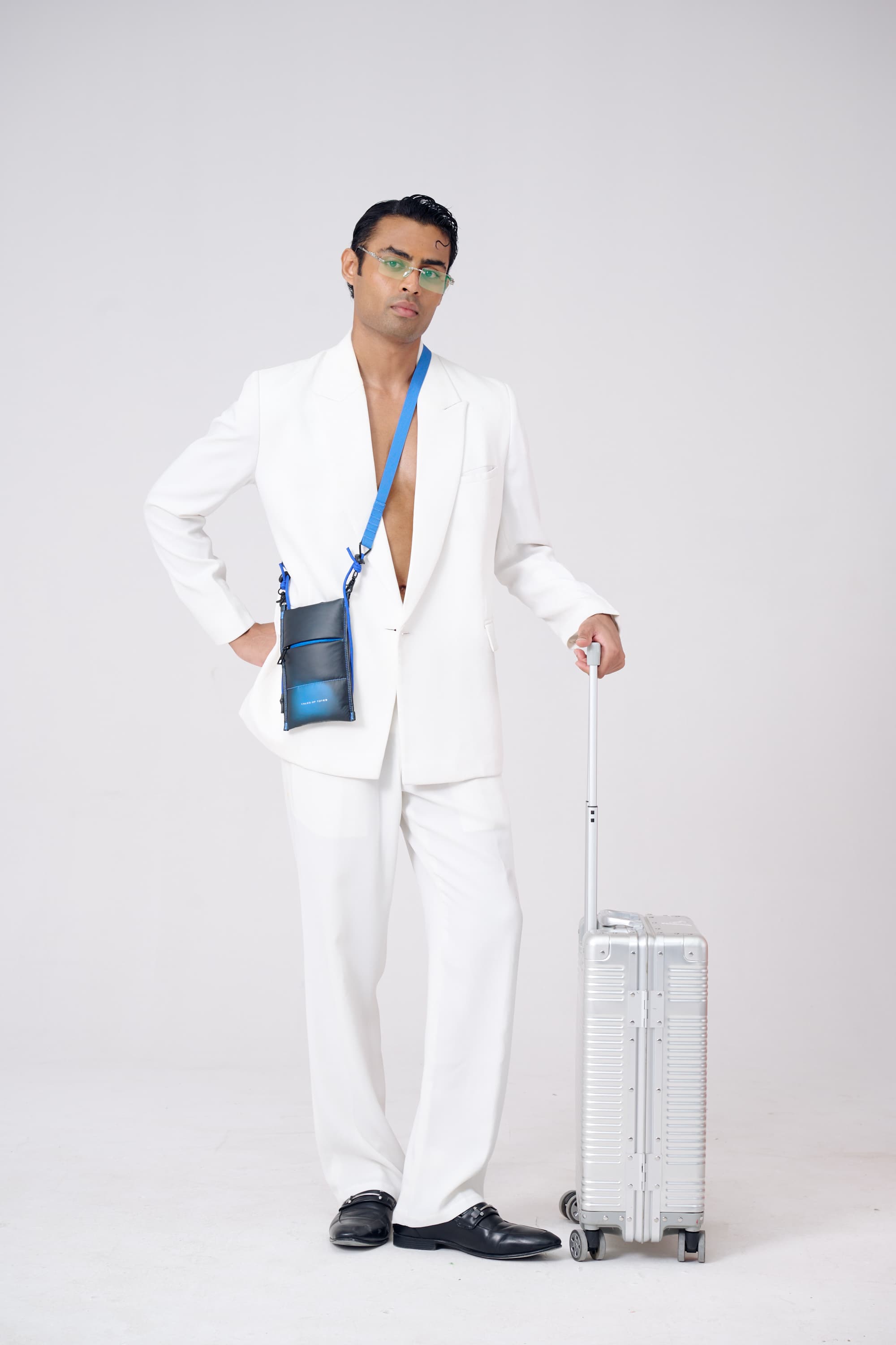 Man in a white suit with a blue lanyard holding a clear suitcase on a white background