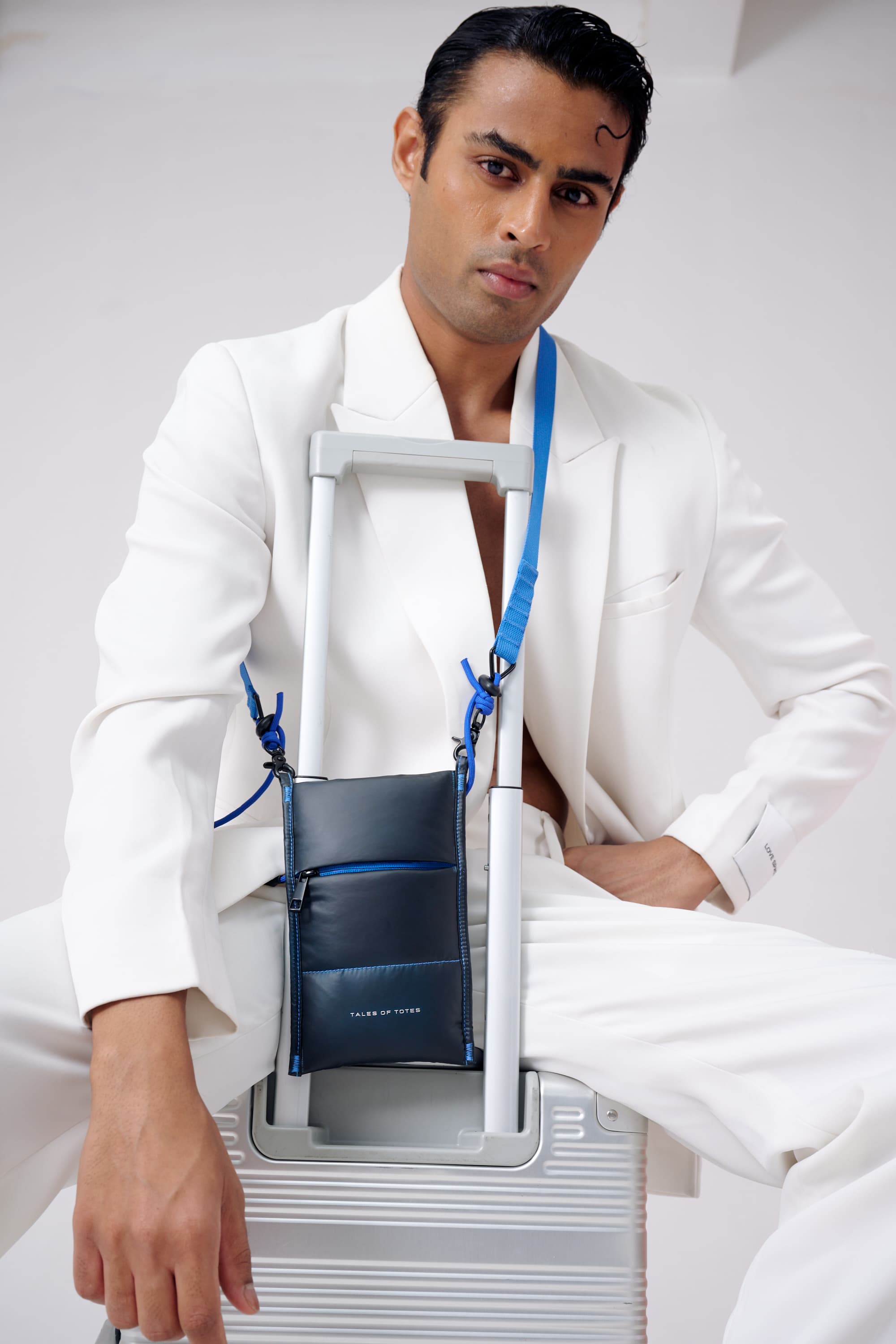 Man in a white suit with a blue bag over his shoulder against a white background
