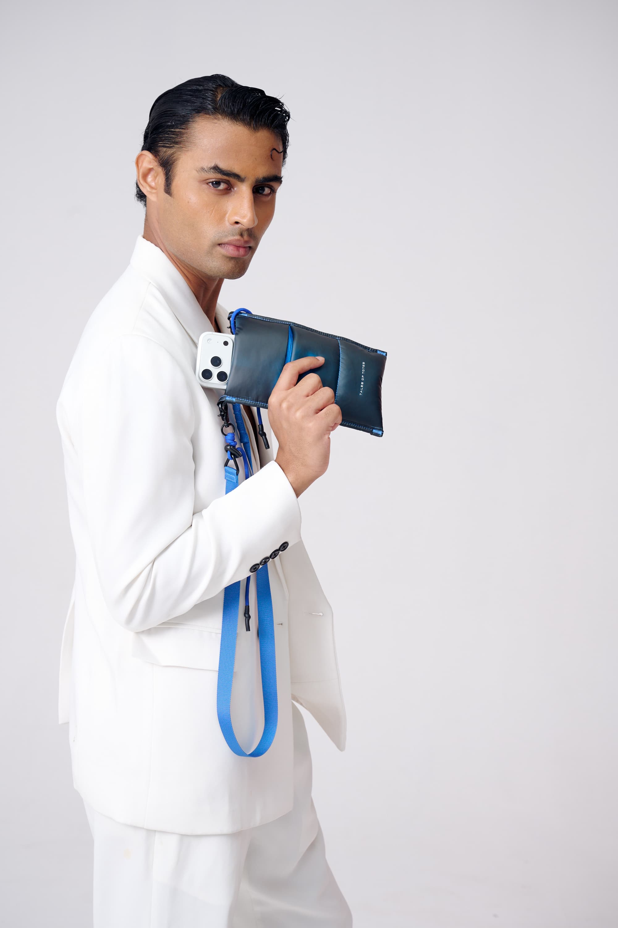Man in a white suit holding a blue and black bag against a white background