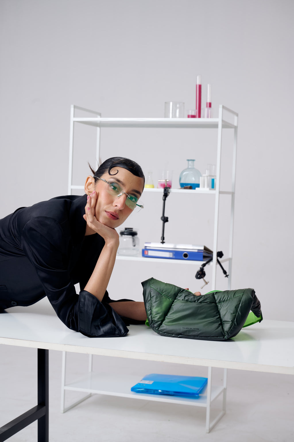 Person with a green bag on a white table against a gray wall with shelves.
